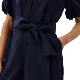 Model wearing Whistles blue dress with puff sleeves, tie waist belt detail and side pocket, shown from waist up.
