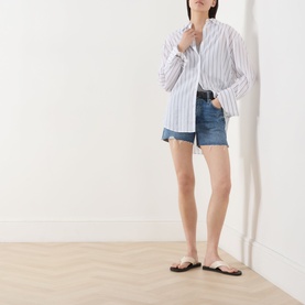 Model wearing Rag & Bone flora denim shorts with white striped oversized shirt and black flat sandals