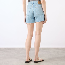 Model wearing Rag & Bone denim shorts in narrows, rear view, with raw-hem cutoff detail, styled with tan flat sandals.