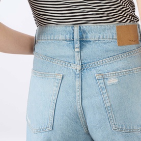 Model wearing Rag & Bone denim shorts in light blue wash with distressed details, styled with a striped top. Back view.