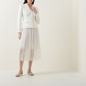Model wearing Self-Portrait cream pleated midi dress with lace hem detail, styled with a white blazer and nude heeled sandals.