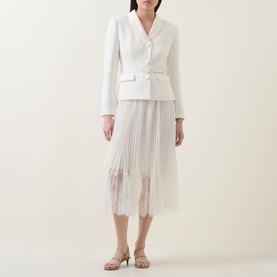 Model wearing Self-Portrait cream dress with structured blazer bodice, pleated midi skirt with lace hem trim, styled with nude heeled mules.