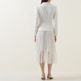 Model wearing Self-Portrait cream dress with structured blazer-style top and pleated tulle midi skirt, shown from the back, styled with brown heeled