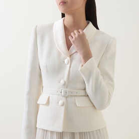 Model wearing Self-Portrait cream textured boucle jacket with belt detail and large buttons, styled with a pleated skirt beneath.