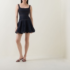 Model wearing Self-Portrait blue denim mini dress with square neckline, sleeveless bodice and broderie anglaise flared skirt, styled with brown flat