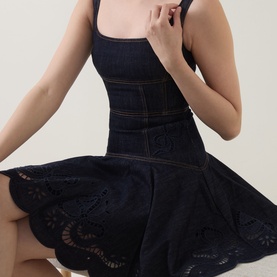 Model wearing Self-Portrait blue denim mini dress with broderie anglaise skirt, square neckline, and fitted bodice with contrast stitching detail.