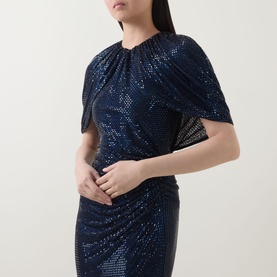 Model wearing Self-Portrait navy blue sequin dress with draped cape sleeve detail and ruched fitted silhouette.