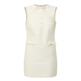 Self-Portrait yellow sleeveless mini dress with bow detail, front buttons, and embellished patch pockets on cream textured fabric.