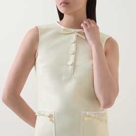 Model wearing Self-Portrait yellow sleeveless dress with bow-detail pockets and button front neckline, in structured polyester fabric.