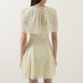 Model wearing Self-Portrait yellow lace mini dress with cape overlay, puff sleeves, fitted waist, and flared skirt, shown from the back.