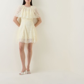 Model wearing Self-Portrait yellow lace mini dress with tiered cape overlay, styled with white heeled mules