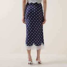 Model wearing Self-Portrait navy polka dot midi skirt with white lace hem trim, styled with white heeled mules. Rear view.