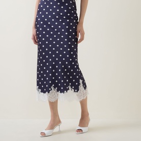 Model wearing Self-Portrait navy polka dot midi skirt with white lace hem trim, styled with white mule heels.