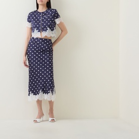 Model wearing Self-Portrait navy polka dot midi skirt with white lace hem trim, styled with matching cropped top and white mules.