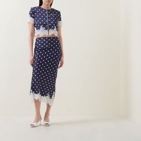 Model wearing Self-Portrait navy polka dot crop top with lace trim, styled with matching midi skirt and white heeled mules.