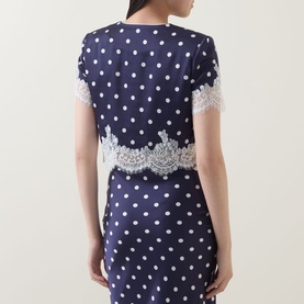 Model wearing Self-Portrait navy polka dot top with white lace hem trim, short sleeves, styled with matching polka dot skirt.