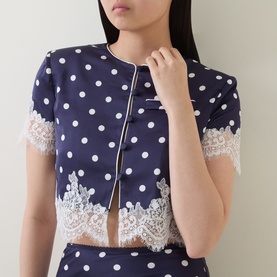 Model wearing Self-Portrait navy polka dot cropped top with white lace hem trim and zip front detail, paired with matching navy skirt.