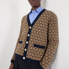 Model wearing Valentino camel wool cardigan with navy V-neck trim, gold buttons, and geometric jacquard pattern, styled with blue shirt and dark