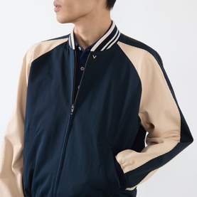 Model wearing Valentino navy casual jacket with beige raglan sleeves, striped ribbed collar, and VLogo detail, styled over polo shirt