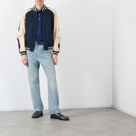 Model wearing Valentino navy varsity casual jacket with cream sleeves and stripe trim, styled with light blue jeans and black loafers