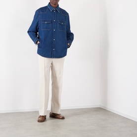 Model wearing Valentino medium blue denim casual shirt with chest pockets, styled with cream trousers and brown loafers.