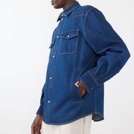 Model wearing Valentino medium blue denim casual shirt with chest pockets, contrast stitching, and tan leather logo tab detail.