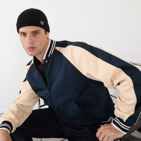 Model with Valentino V-Logo Rib Knit Beanie Hat in black cashmere with turned-up brim, styled with navy and cream varsity jacket.