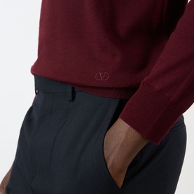Model wearing Valentino Logo Knitted Polo Sweater in red wool with embroidered VLogo, styled with navy tailored trousers.
