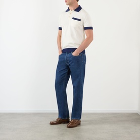 Model wearing Valentino medium blue denim jeans in straight leg fit, styled with a cream and navy polo shirt and brown loafers.