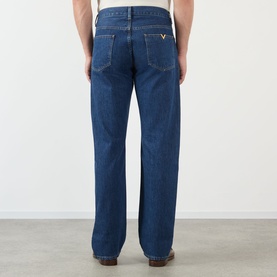 Model wearing Valentino medium blue denim jeans, rear view showing gold V logo hardware on back pocket, straight-leg fit