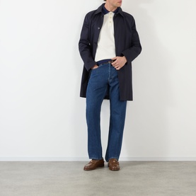 Model wearing Valentino medium blue denim jeans in cotton, styled with a navy overcoat, cream polo shirt and brown loafers.