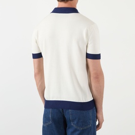 Model wearing Valentino cream cotton polo shirt, back view, navy blue contrast collar, cuffs and hem, paired with blue denim jeans