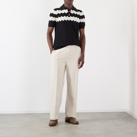 Model wearing Valentino black cotton polo with white zigzag knit yoke, styled with cream tailored trousers and brown leather loafers.