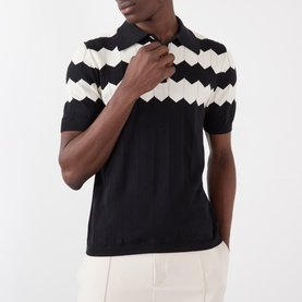 Model wearing Valentino black cotton polo shirt with zigzag chevron wave intarsia knit panel across chest and collar, paired with cream trousers