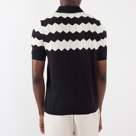 Model wearing Valentino black cotton polo shirt with cream zigzag geometric pattern across chest and shoulders, short sleeves.