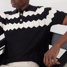 Model wearing Valentino black cotton polo with bold white chevron zigzag textured panel across chest and collar detail