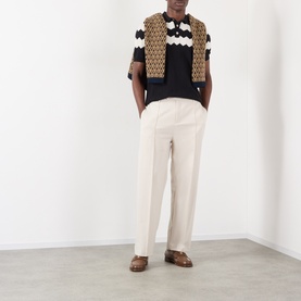Model wearing Valentino black cotton polo with tan and white crochet pattern, styled with cream trousers and brown loafers