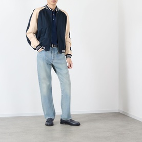 Model wearing Valentino indigo cotton polo shirt, styled with navy varsity jacket, light wash jeans, and dark loafers.