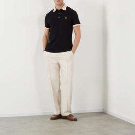Model wearing Valentino V-Logo Polo Shirt in black with contrast cream collar and cuffs, styled with cream trousers and brown loafers.