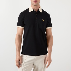 Model wearing Valentino V-Logo Polo Shirt in black with contrasting cream collar and cuffs, gold V-logo, styled with beige trousers.
