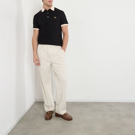 Model wearing Valentino V-Logo Polo Shirt in black with contrast collar and cuffs, styled with cream trousers and brown loafers.