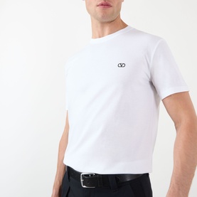 Model wearing Valentino white cotton T-shirt with small VLogo emblem on chest, styled with black trousers and belt.
