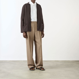 Model wearing Valentino Pleated Straight-Leg Trousers in camel, styled with a dark brown blazer and white shirt, brown sandals.