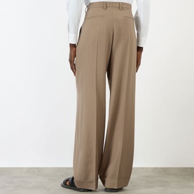 Model wearing Valentino Pleated Straight-Leg Trousers in camel, high-rise with pressed creases and turn-up hems, styled with a white shirt.