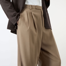Model wearing Valentino Pleated Straight-Leg Trousers in camel, high-rise with pressed creases and turn-up hems, styled with a dark brown jacket.