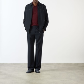 Model wearing Valentino Pressed Slim-Leg Trousers in storm blue, styled with a dark zip jacket, burgundy knit and black loafers.