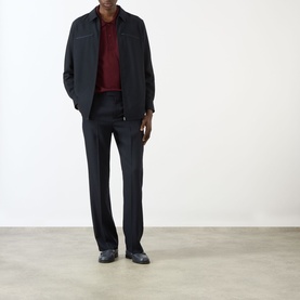 Model wearing Valentino Pressed Slim-Leg Trousers in storm blue wool, styled with a dark zip jacket and burgundy knitwear.