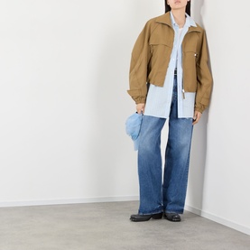 Model wearing Acne Logo Technical Bomber Jacket in dark khaki with blue wide-leg jeans and light blue shirt, carrying a small blue bag.