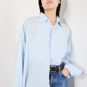 Model wearing Acne blue striped oversized shirt in lyocell, styled with black belt and blue jeans