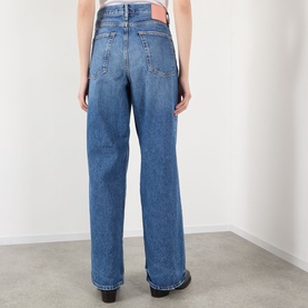 Model wearing Acne 1981 U Vintage Wide-Leg Jeans in mid blue, rear view showing logo patch, wide leg, and clean hems.